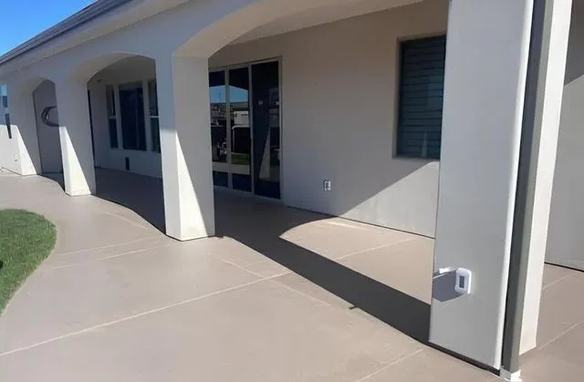 Covered patio with tan concrete flooring and white pillars.
