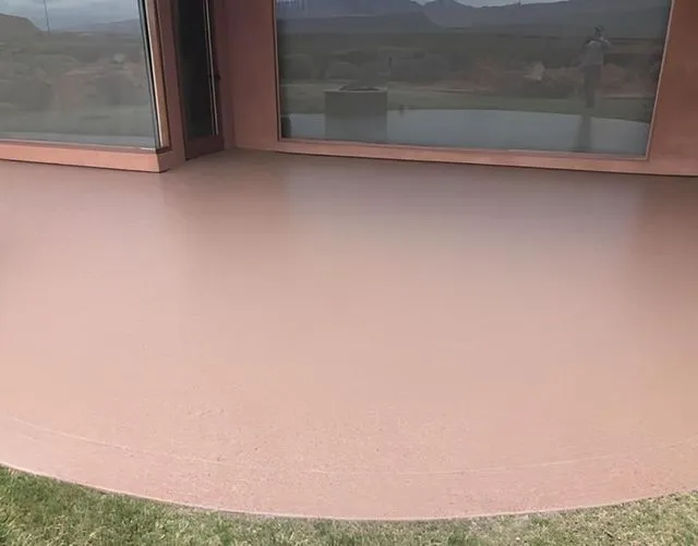 Reddish-brown concrete patio with sliding glass doors. Curved edge meets green grass.