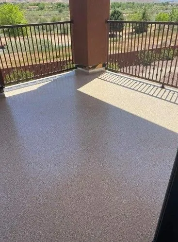 A balcony with a brown and tan speckled floor and a metal railing overlooks a scenic landscape.