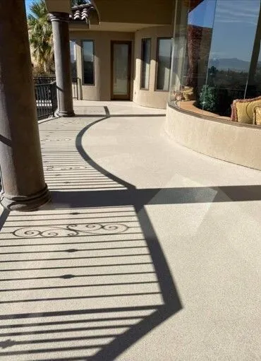 Beige curved walkway with shadows from a decorative railing. Pillars support the overhang.