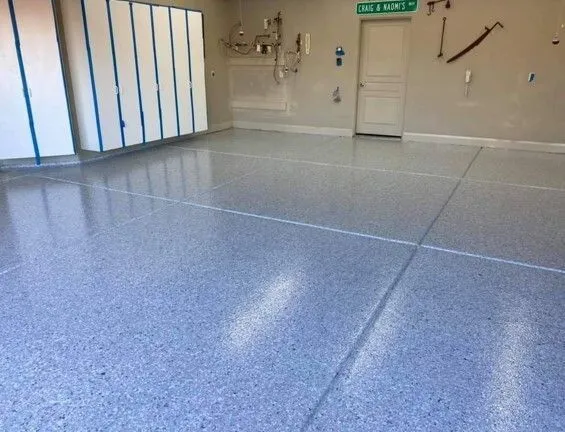 A garage interior with a shiny, speckled epoxy floor. White cabinets and a door are visible.