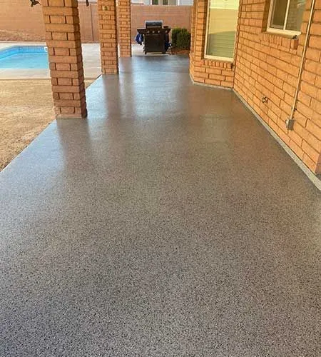 A covered outdoor patio with a glossy speckled gray concrete floor, brick columns, and a view of a pool.