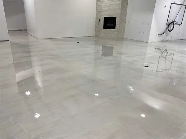 Shiny, light gray epoxy floor in an empty room, reflecting surrounding white walls and a fireplace.