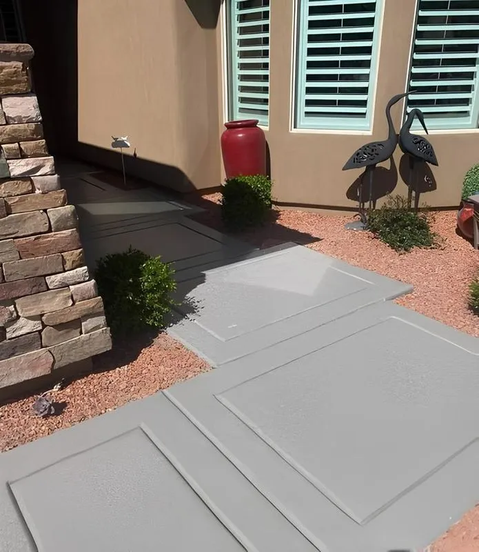 Stone pathway leading to a beige house entrance. Red gravel, plants, and metal bird sculptures are in the yard.