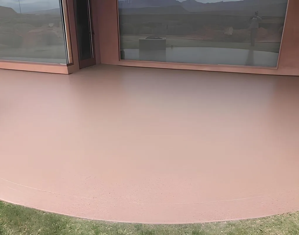A smooth, rose-colored concrete patio with large windows in the background and a grassy lawn.