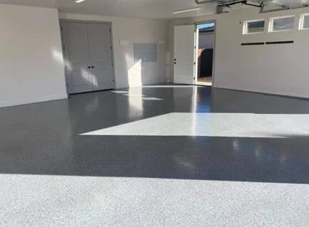 A bright, spacious garage with a glossy epoxy floor. Sunlight streams in, illuminating the white walls and closed doors.