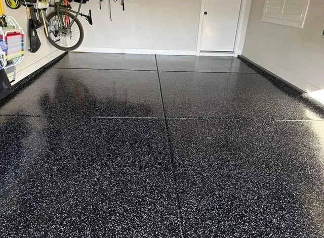 Garage floor with a speckled, black epoxy coating. A bicycle is mounted on the wall.