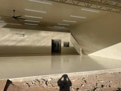 Interior of a large, empty, beige-colored room with a polished floor. Stairs and a doorway are visible. A ceiling fan is mounted.
