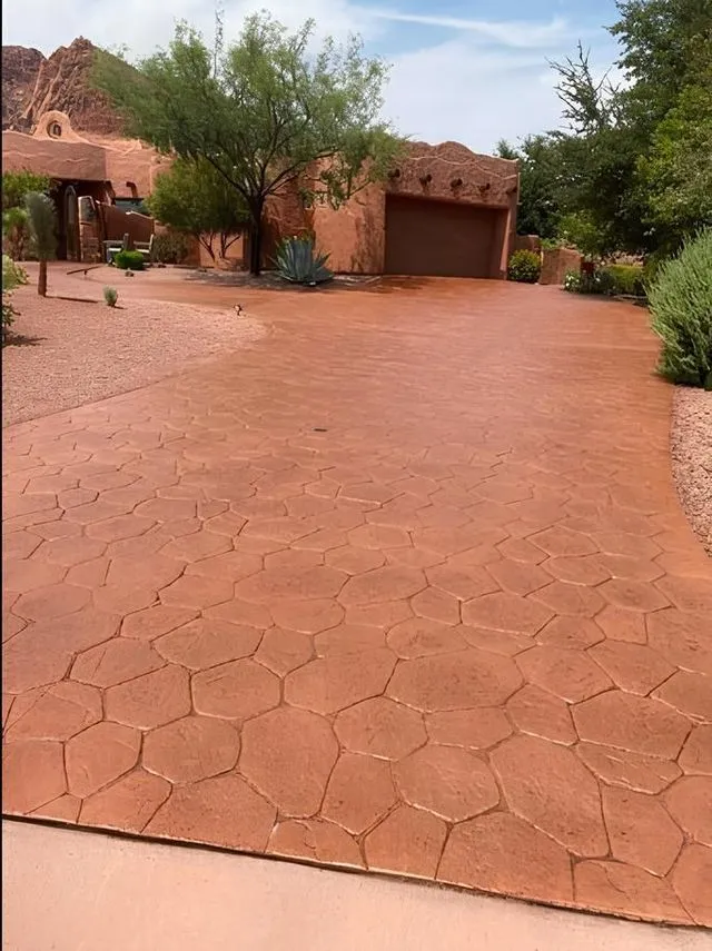 Red-toned, textured driveway leading to a Spanish-style house with a garage and landscaping.