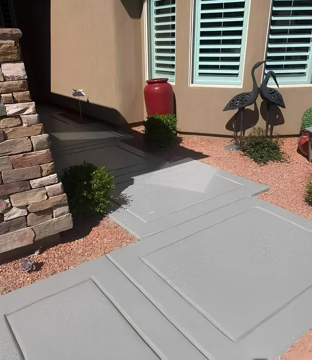 Gray concrete pathway leading to a doorway, flanked by landscaping and decorative metal birds.